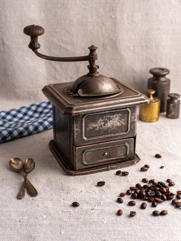 Antique French Peugeot Frères tinned steel coffee mill with coffee beans and vintage spoon accents.