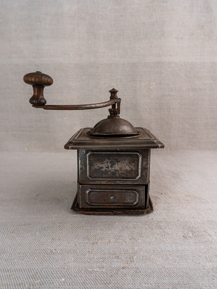 Antique French Peugeot Frères coffee mill, tinned steel with wooden handle, on neutral fabric surface.