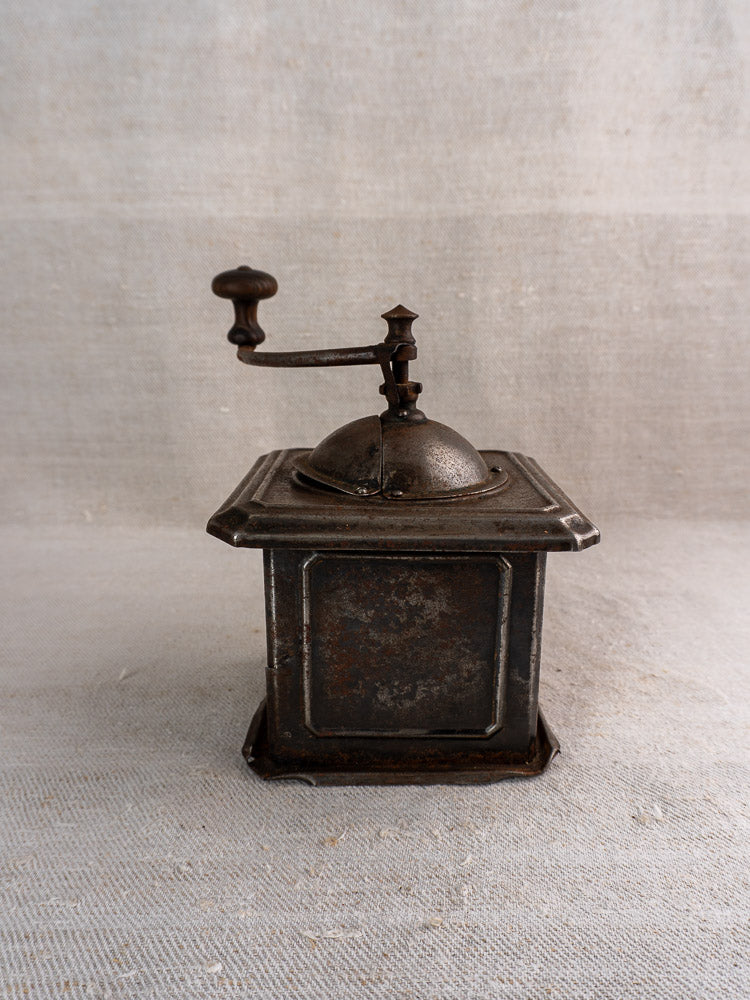 Antique French Peugeot Frères coffee mill, tinned steel, square base, hand crank, on light fabric.