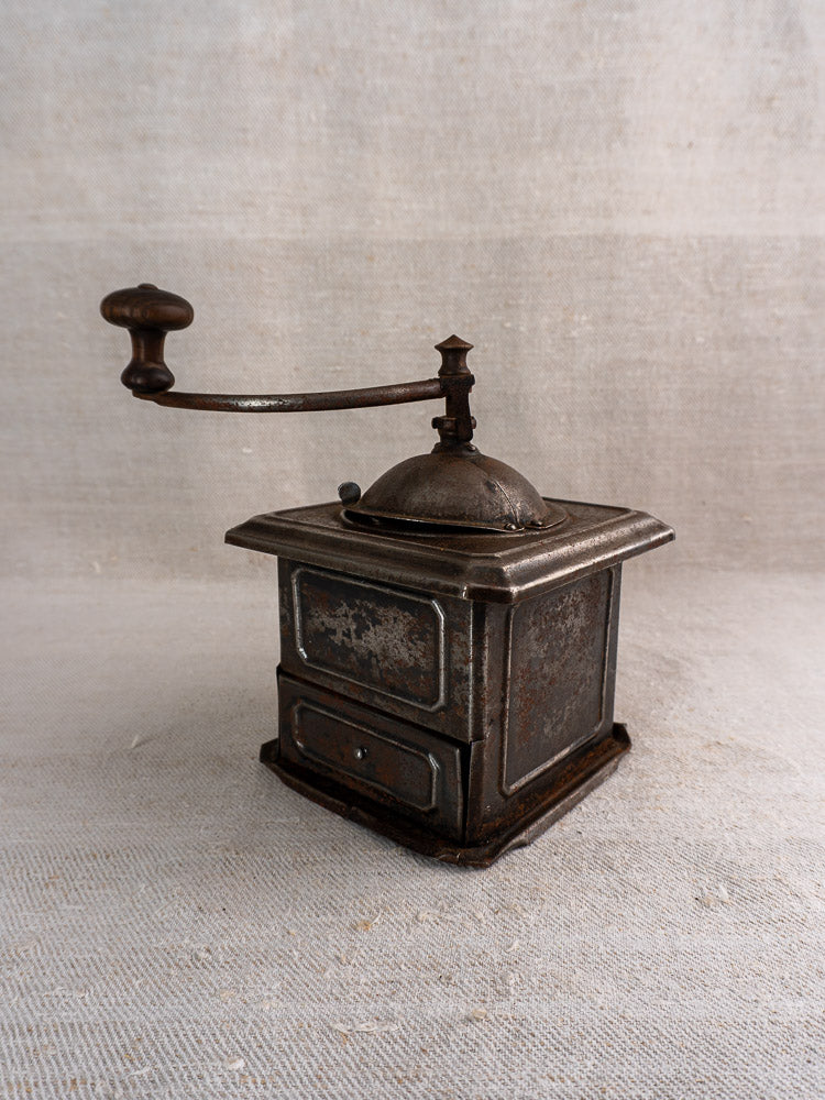 Antique French Peugeot Frères tinned steel coffee mill with wooden handle, aged patina on beige textured surface.