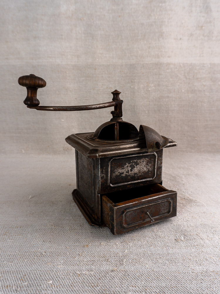 Antique French Peugeot Frères coffee mill in tinned steel with wood handle, shown on beige fabric.