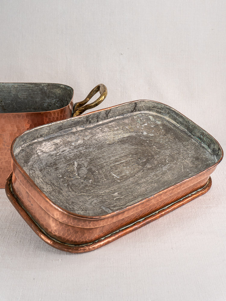 Hand-hammered 19th-century French copper daubière with brass handles on a matching copper tray, silvery interior showing.