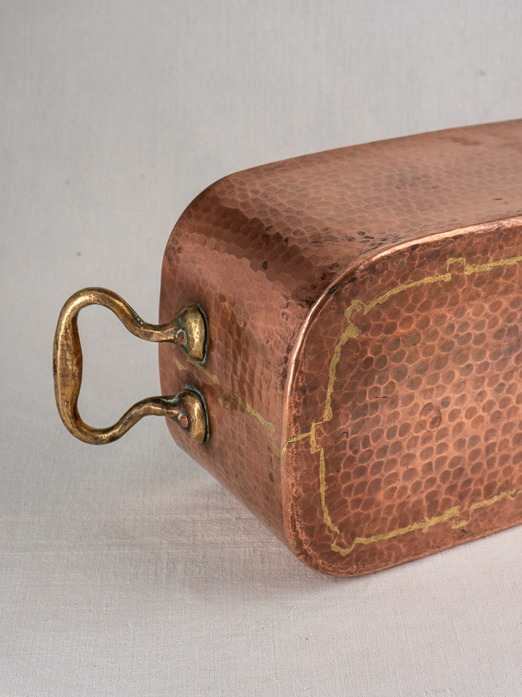 Antique French copper daubière, 19th-century, hand-hammered with brass handle, textured surface and seams on light background.
