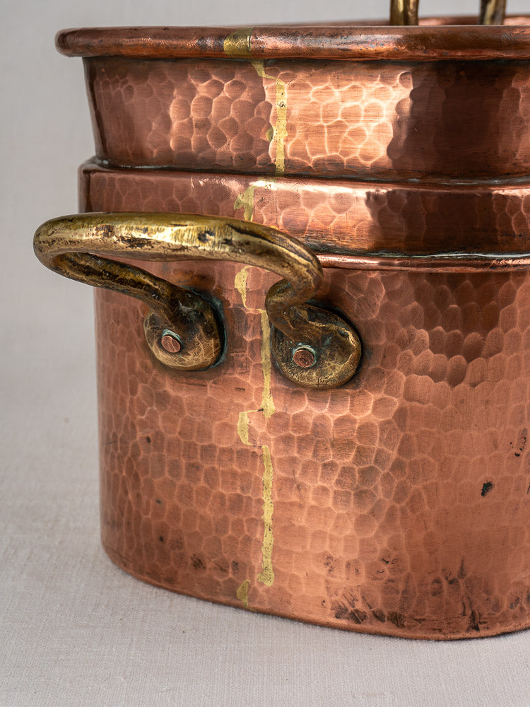 Antique French copper daubière with brass handle, hand-hammered finish, and distinct gold-colored vertical repair line.
