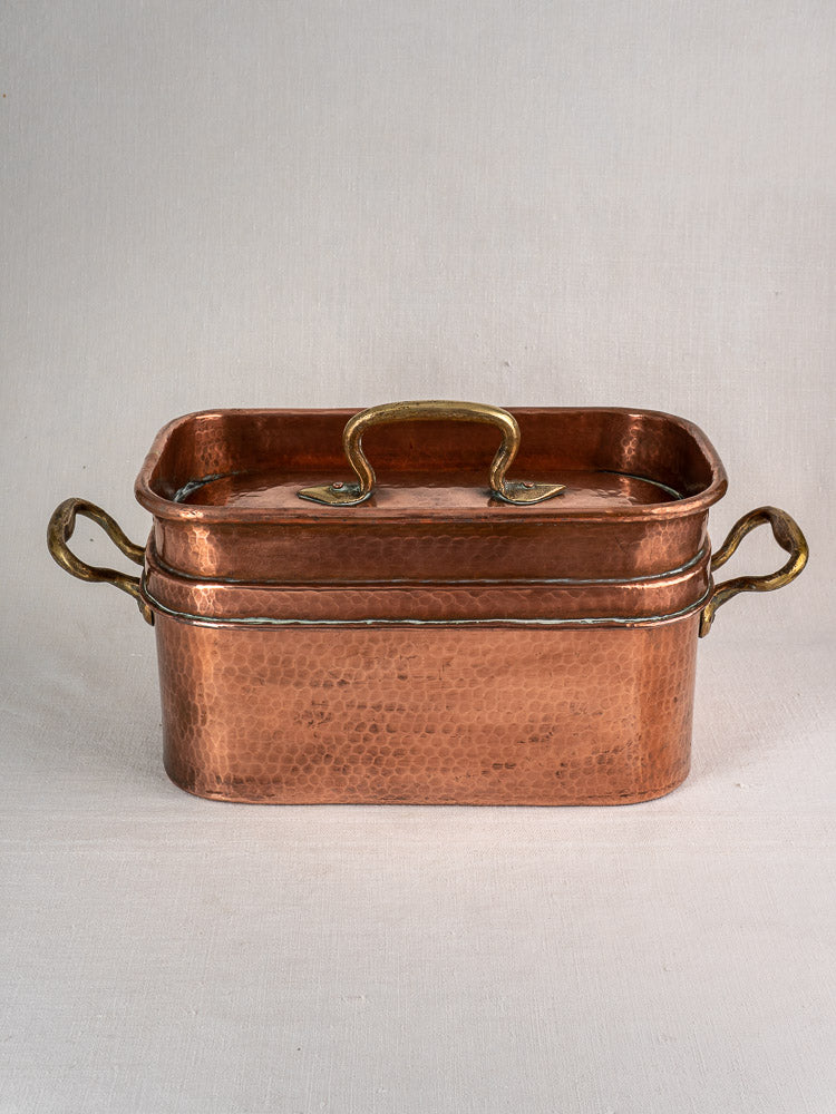 Antique French copper daubière, large 19th-century hand-hammered pan with lid and brass handles, on plain background.