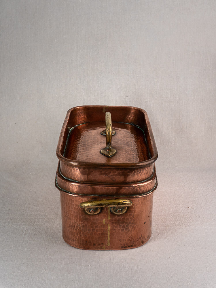 Large antique French copper daubière with hand-hammered finish, brass handle, patina, lid, on neutral gray surface.