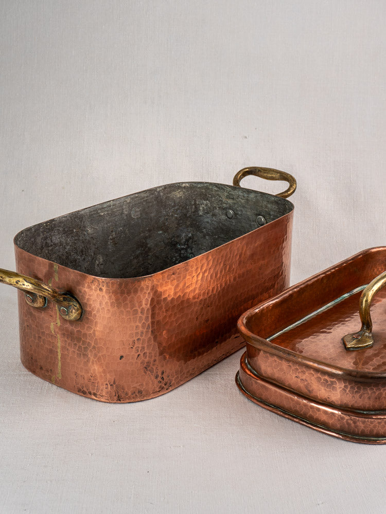 Antique French copper daubière with lid beside another copper Dutch oven on a light surface.