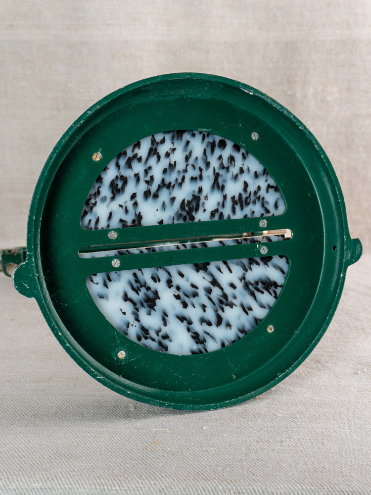 Vintage French Roquefort cheese cutter, green circular design with metal blade, speckled surface on beige fabric.