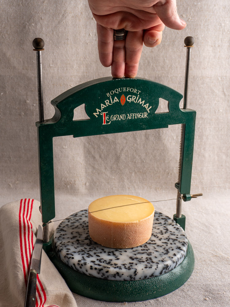 Vintage French Roquefort cheese cutter by Maria Grimal Fromagerie, 1960s, on speckled marble with striped cloth.