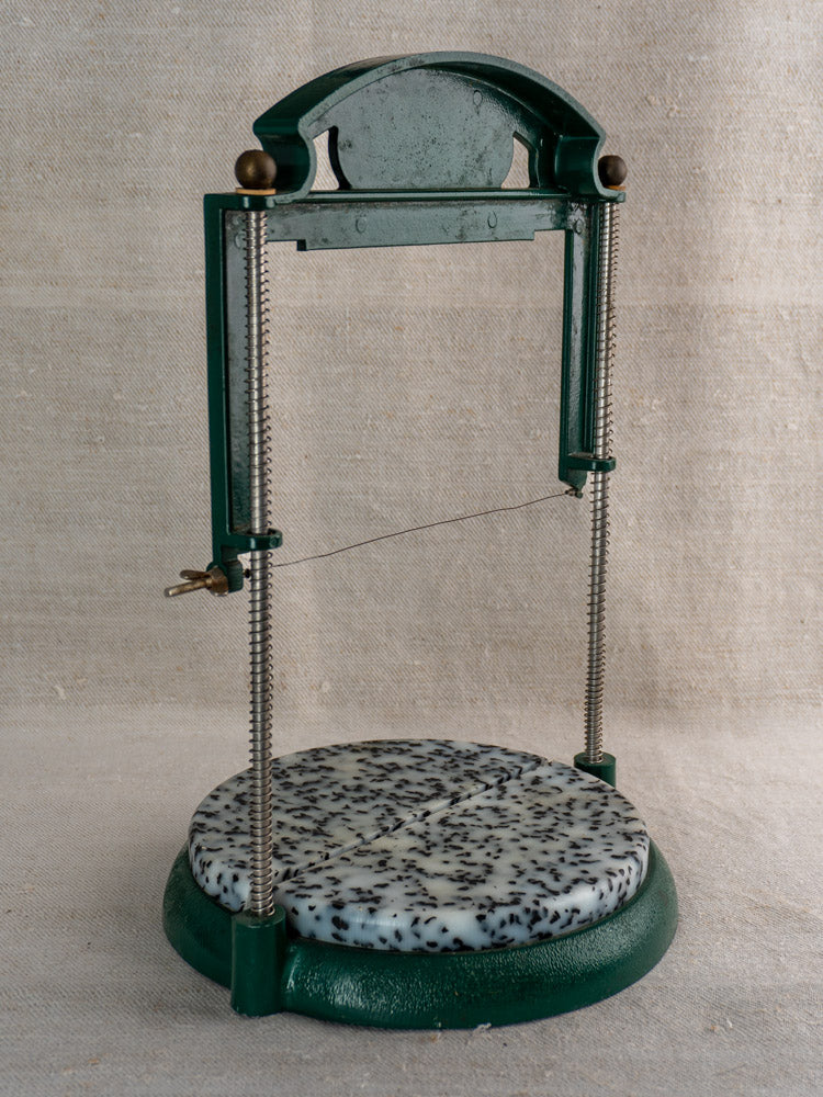 Vintage French Roquefort cheese cutter, 1960s, green frame, speckled platform, on neutral fabric background.