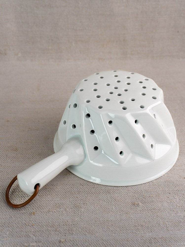 Vintage French porcelain berry strainer with copper ring, shown upside down on neutral fabric.