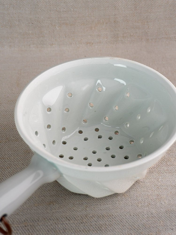 Vintage French porcelain colander with copper ring and draining holes on a textured beige surface.