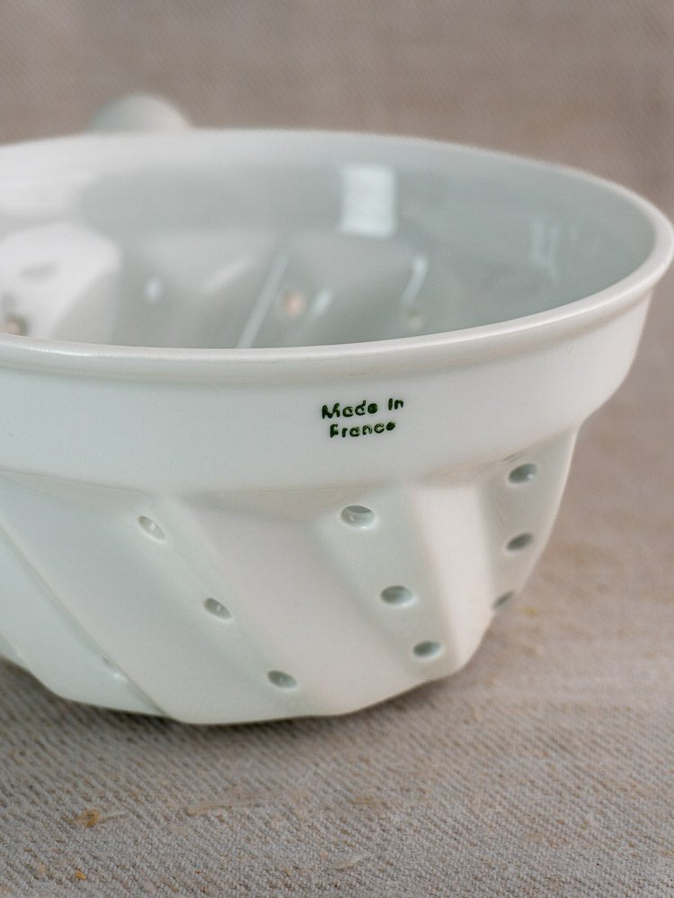 Vintage French porcelain colander with copper ring and green “Made in France” print, on beige surface.