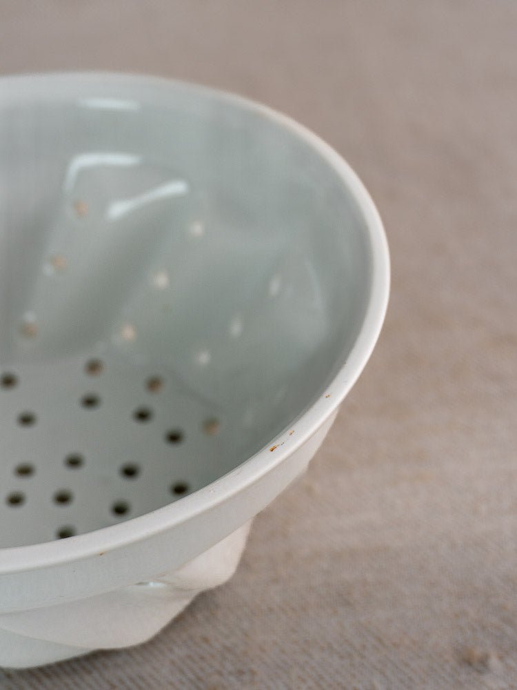 Vintage French porcelain berry strainer with copper ring and small drainage holes on beige fabric.