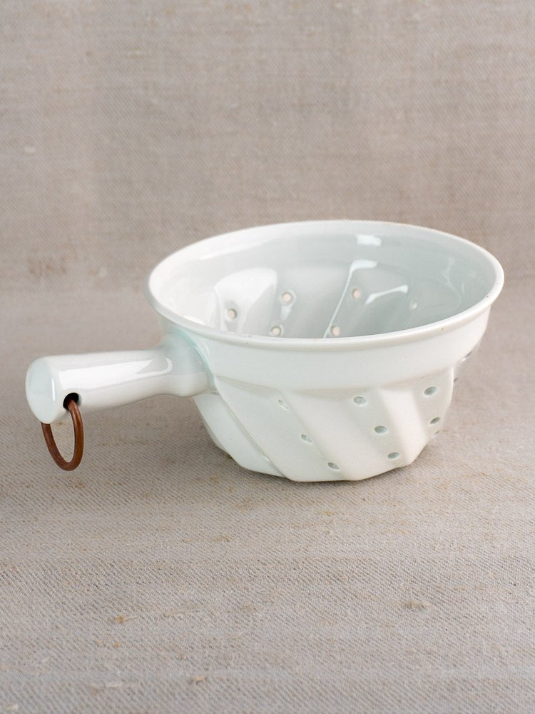 Vintage French porcelain colander with copper ring, ridged bowl, and drainage holes on neutral surface.