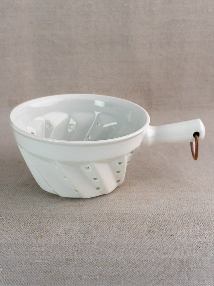 Vintage French white porcelain berry colander with copper ring, displayed on textured beige surface.
