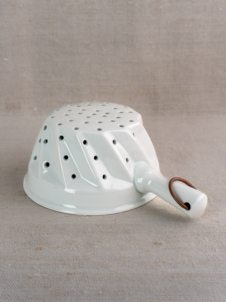 Vintage French porcelain colander with copper ring, upside down on beige fabric, handle and holes visible.