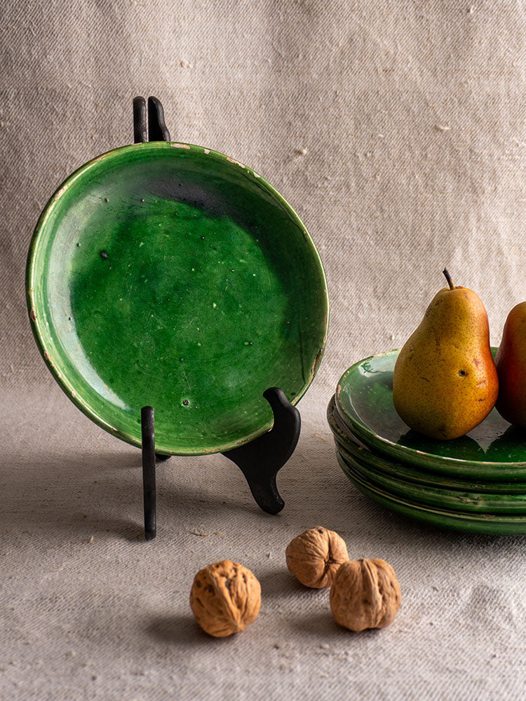 Set of five antique French green glazed earthenware plates on black stand with pears, walnuts, and brocante accents on beige fabric.