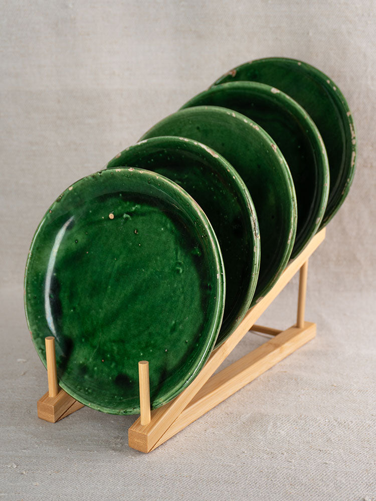 Set of five antique French green glazed earthenware plates in a wooden rack on textured fabric.