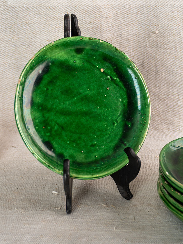 Antique French green glazed earthenware plate on black stand, set of five, beige textured fabric backdrop.