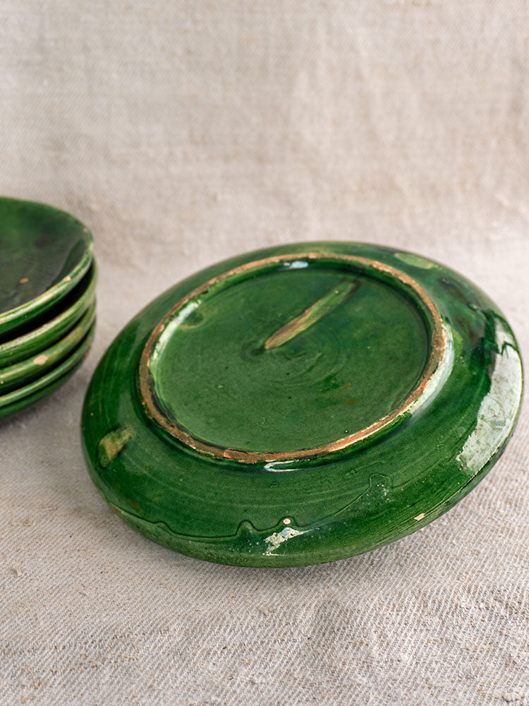 Set of five antique French green glazed earthenware plates, one showing terre vernissée base on beige fabric.