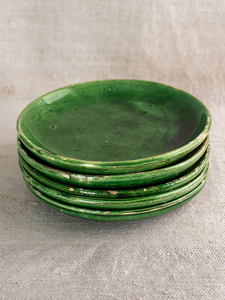 Set of five antique French green glazed earthenware plates with rustic patina on textured beige fabric.