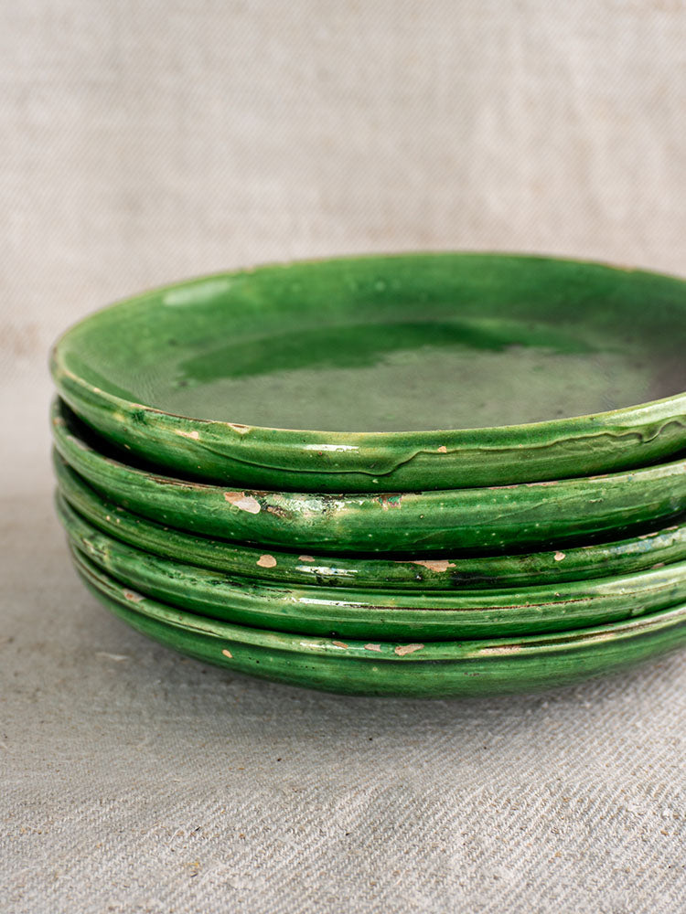 Set of five antique French green glazed earthenware plates on a textured, light fabric surface.