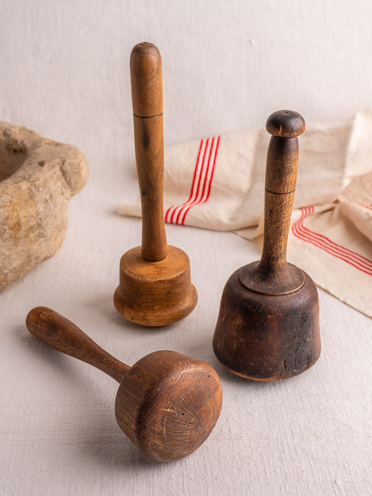 Set of three antique French wooden mallets with varied shapes and wood tones on a light gray fabric background.