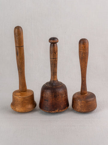 Set of three antique French wooden mallets with varied shapes and wood tones on a light gray fabric background.
