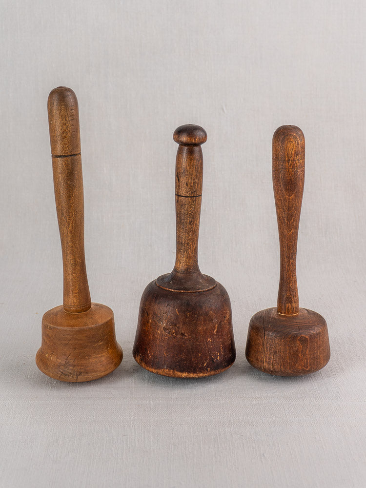 Set of three antique French wooden mallets with turned handles, vintage wear, displayed upright on light gray fabric.