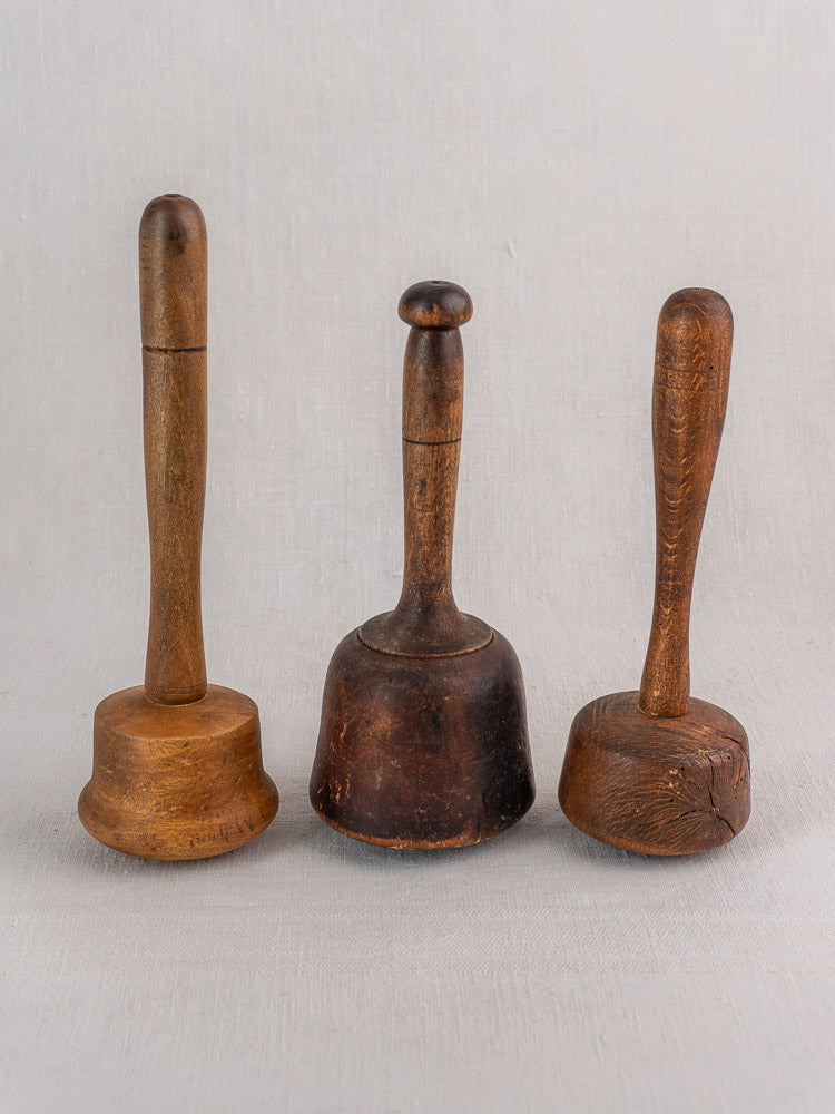 Set of three antique French turned hardwood mallets with vintage handles, worn bases, and wood grain on neutral fabric.
