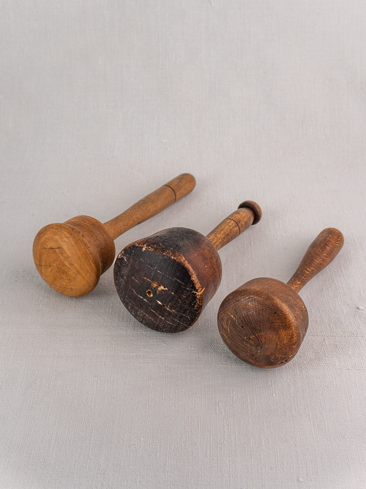 Set of three antique French wooden mallets in turned hardwood, each with unique wear, on a light grey surface.