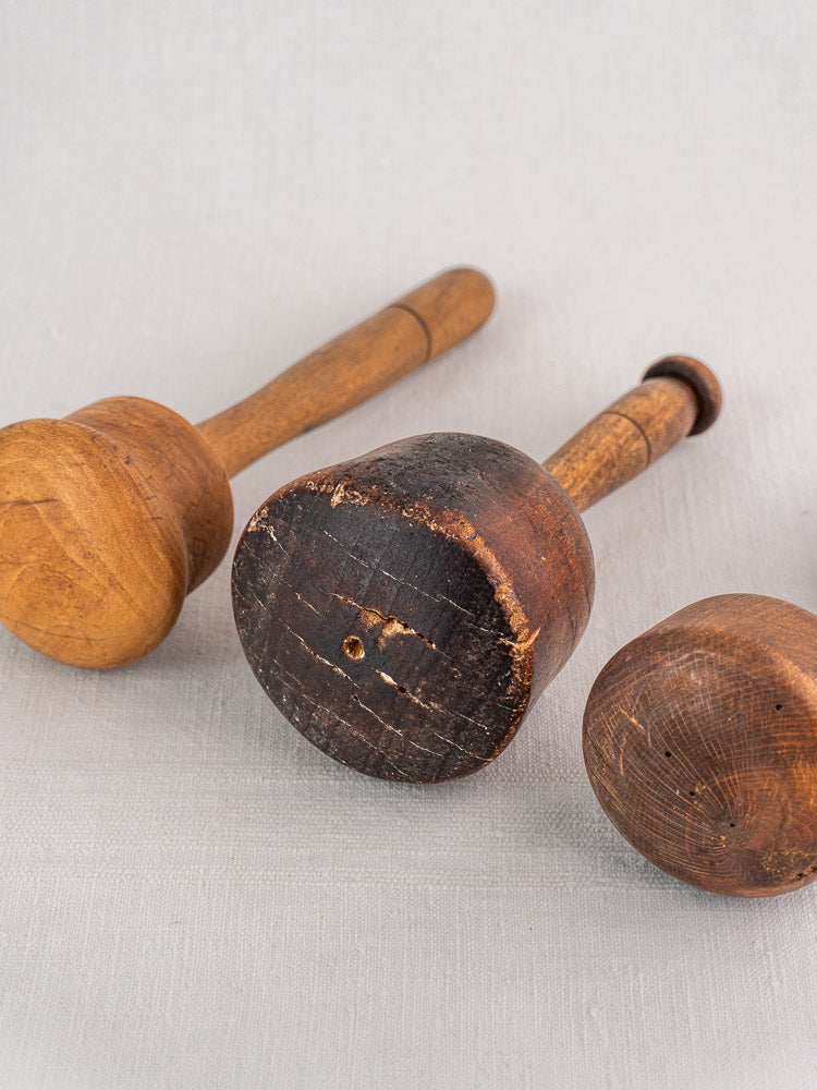 Set of three antique French turned hardwood mallets with varied patina on a light fabric background.