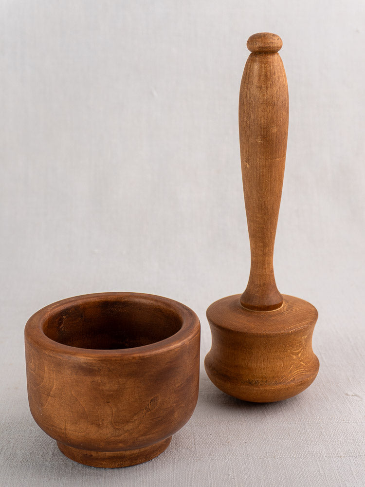 Antique French wooden mortar and pestle with round shallow bowl and curved handle on light gray surface.
