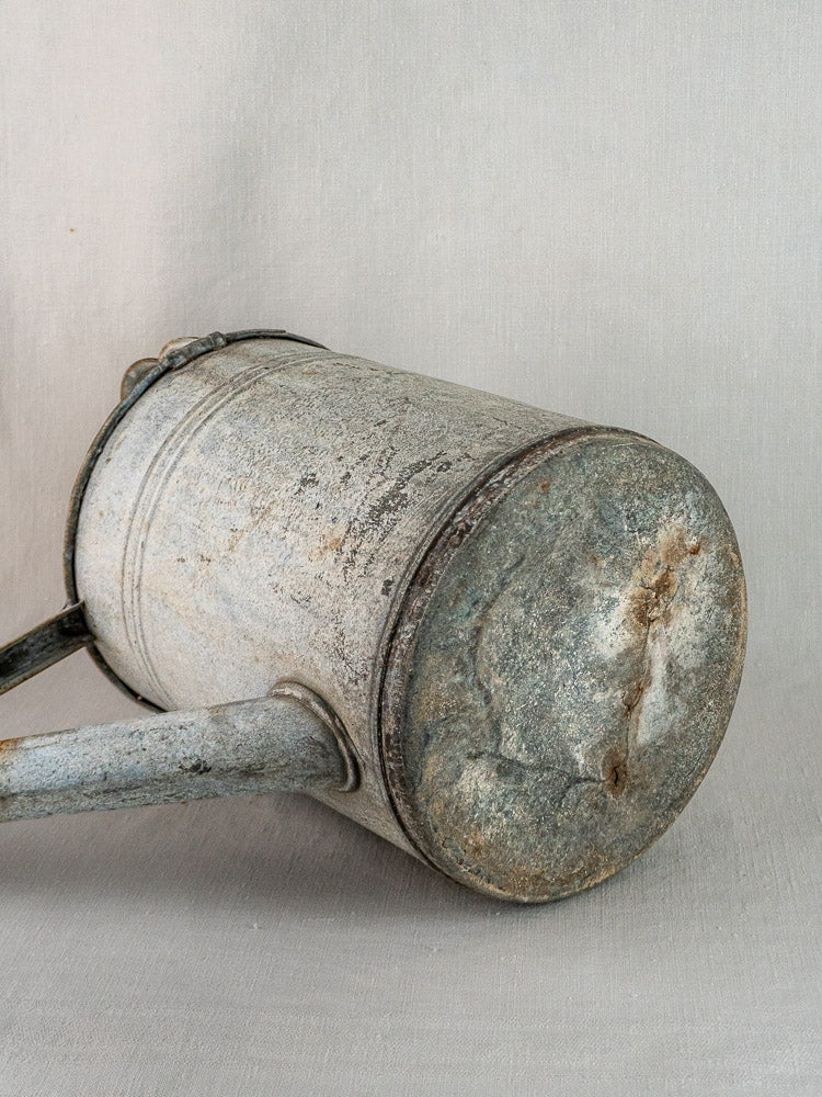 French zinc watering can with aged patina and rust, vintage garden decor against neutral background.