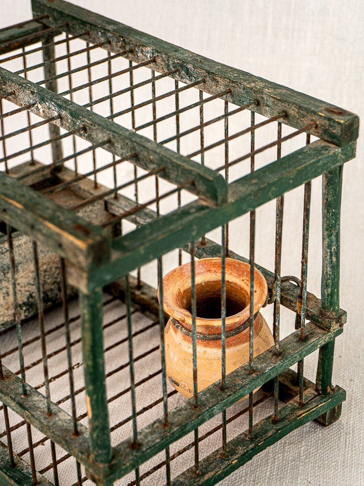 Antique French green painted wood and wire bird cage with terracotta cup, set on a light textured surface.